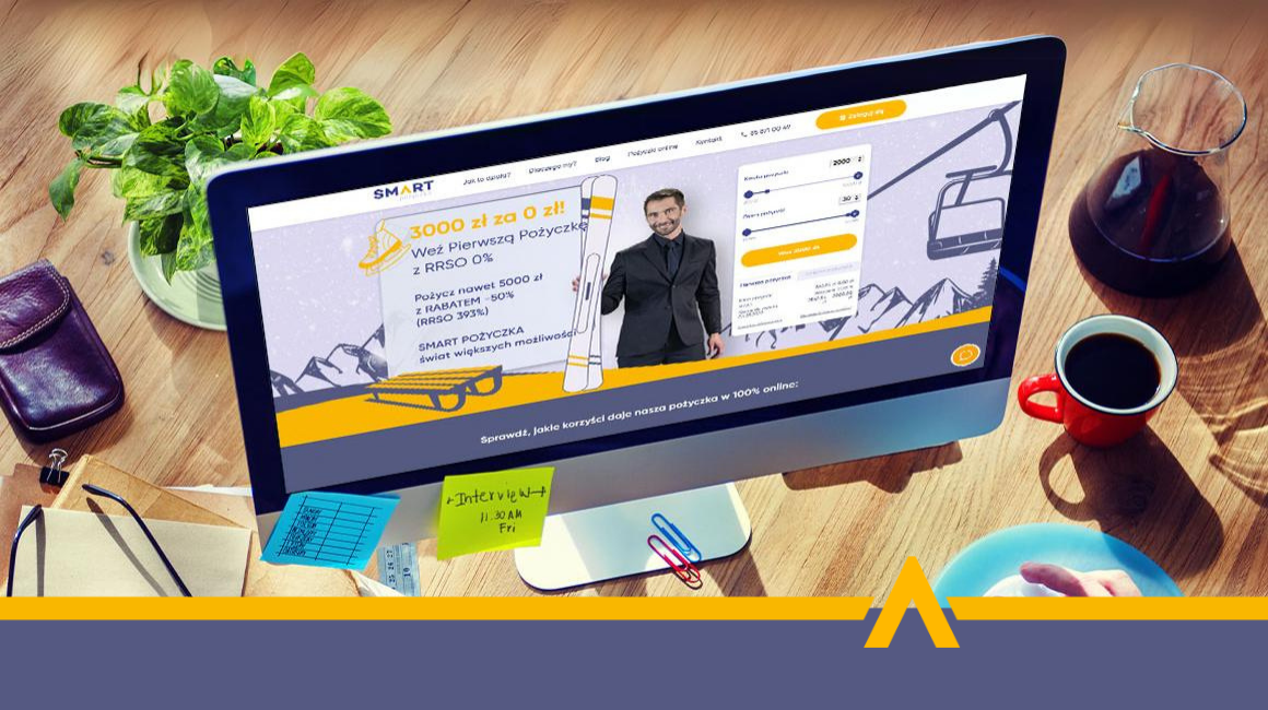 Ekran komputera z otwartą stroną internetową oferującą pożyczkę online z RRSO 0%, na biurku z kawą, notatkami i rośliną.