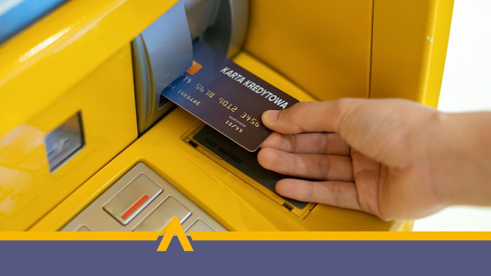 Ręka wkładająca kartę do żółtego bankomatu