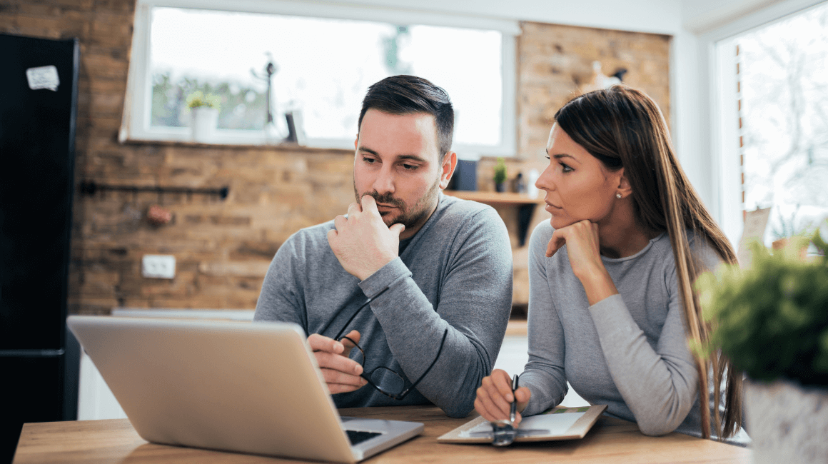 Para siedząca przy stole w domu, wspólnie analizująca dokumenty i informacje na laptopie.